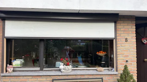 Volet blanc partiellement abaissé sur une façade en briques